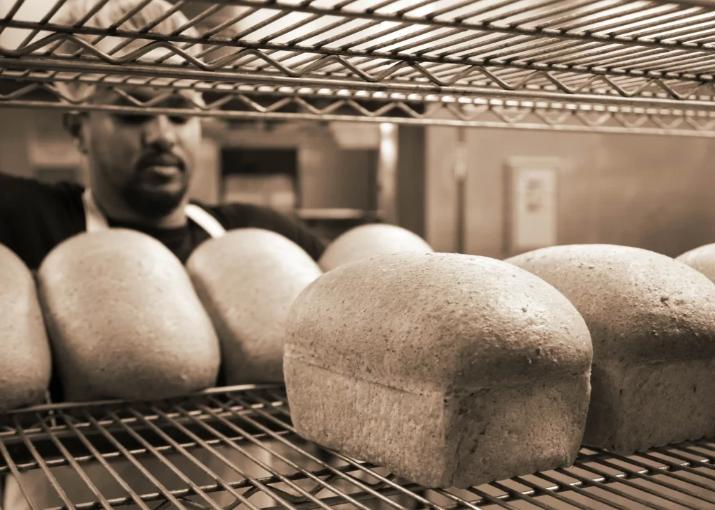 A baker puts bread onto racks.