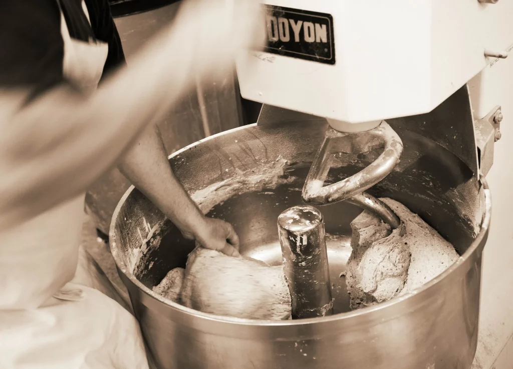 A person is mixing dough in an industrial mixer.